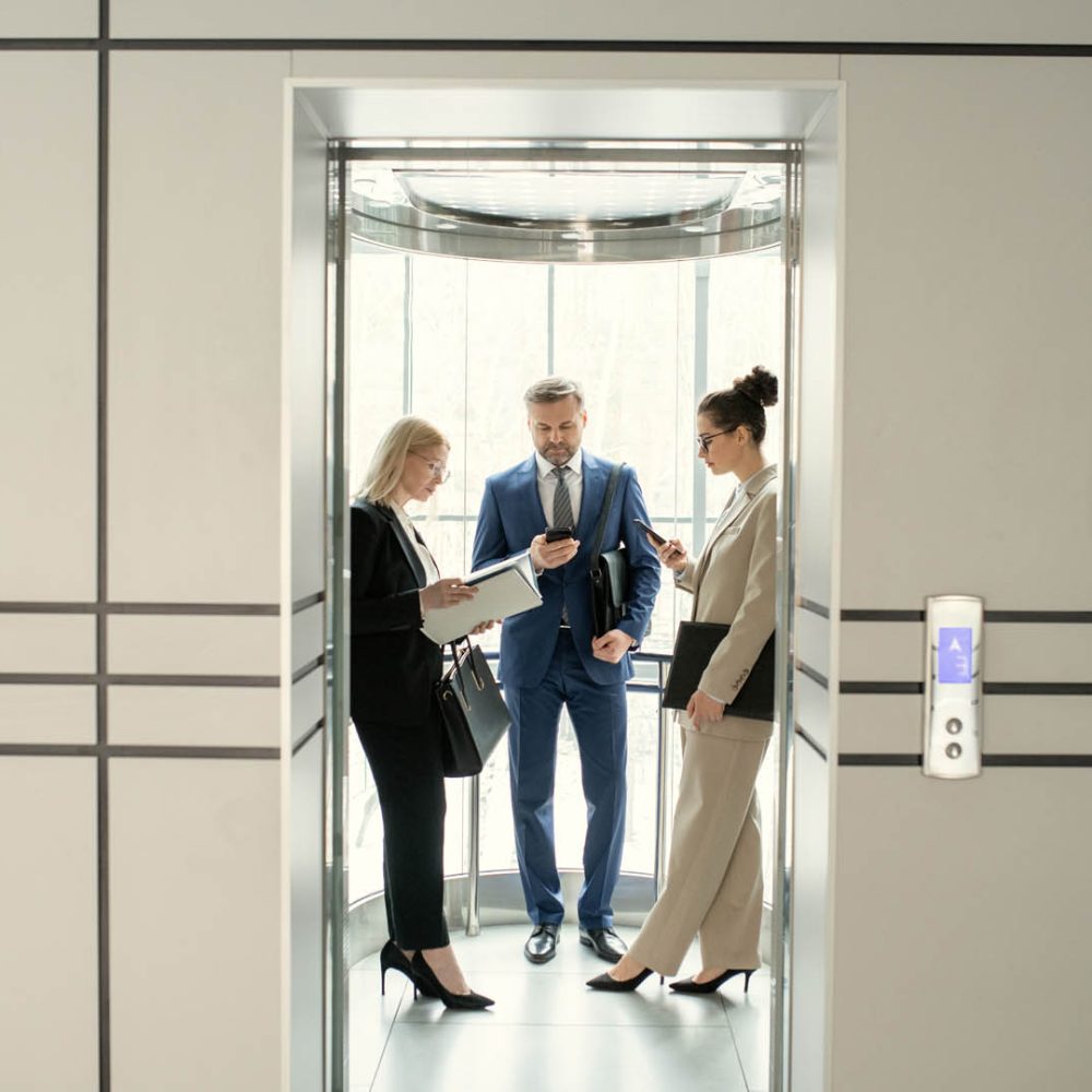 Serious business people standing in elevator and preparing for meeting or surfing net on gadgets