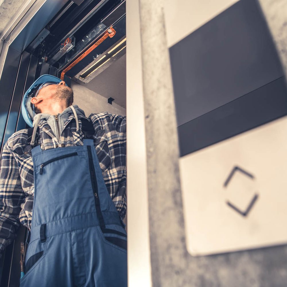 Professional Caucasian Elevator Technician Fixing Lift Doors in Newly Build Residential Building. Lifting Machine Maintenance.