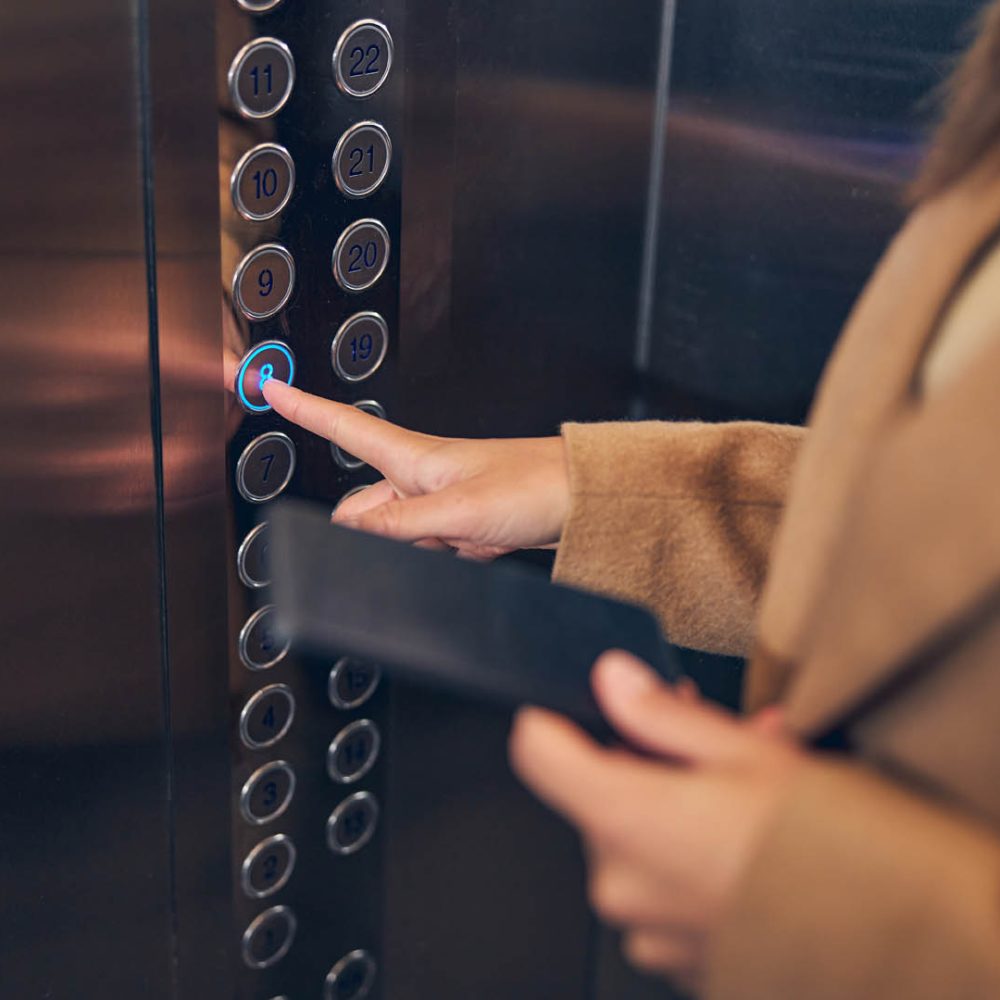 Close up photo of woman in brown coat pressing button of the lift to go down